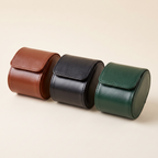 Les trois coloris de l’étui de voyage Escale côte à côte : cognac, noir et vert foncé, fermés